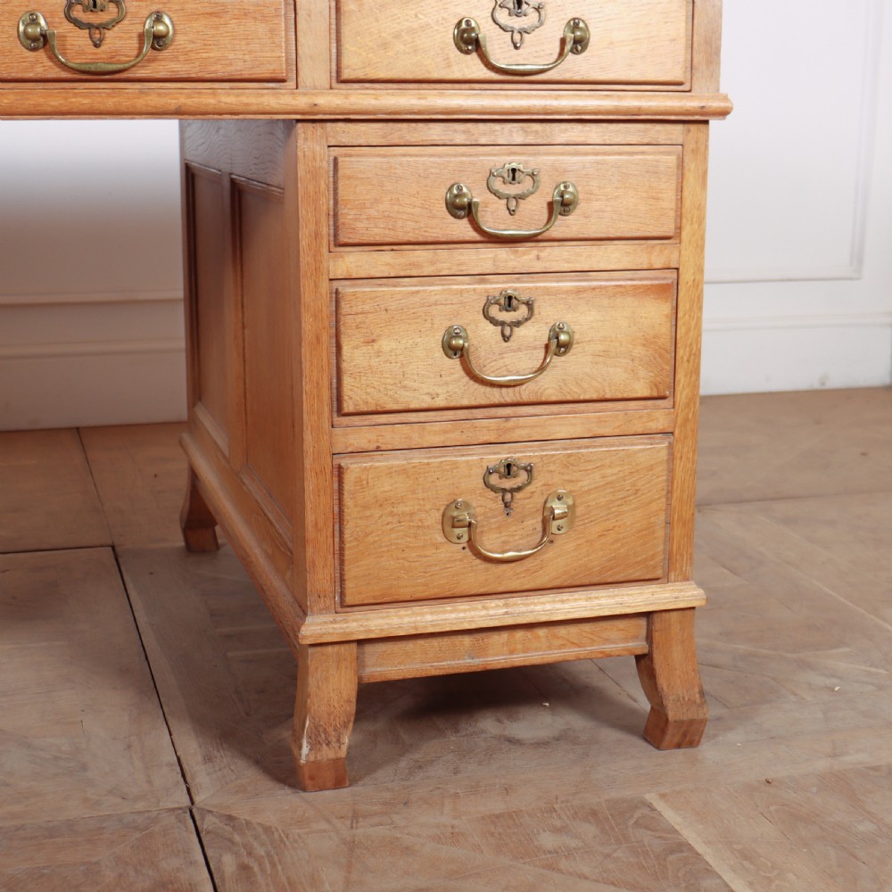 An antique pale oak pedestal desk featuring ten drawers with brass drop handles and a dark leather inset writing surface. View III