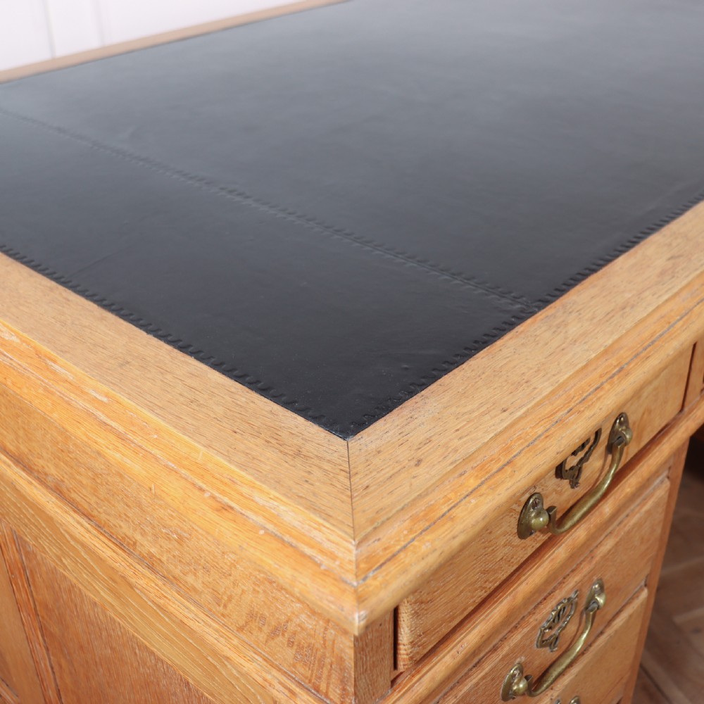 An antique pale oak pedestal desk featuring ten drawers with brass drop handles and a dark leather inset writing surface. View VIII
