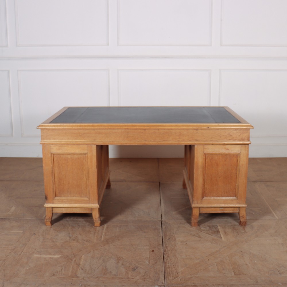 An antique pale oak pedestal desk featuring ten drawers with brass drop handles and a dark leather inset writing surface. View IX