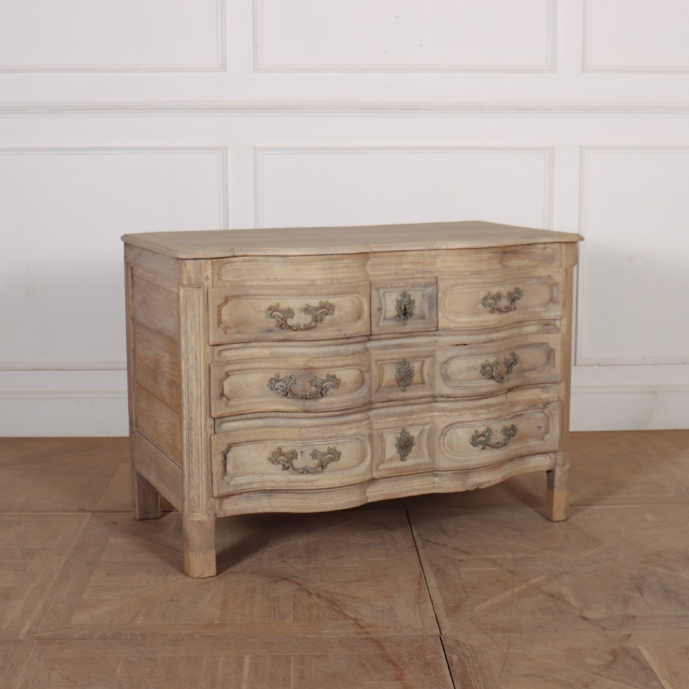 An 18th-century bleached oak French commode with three moulded serpentine drawers featuring brass handles and key escutcheons.