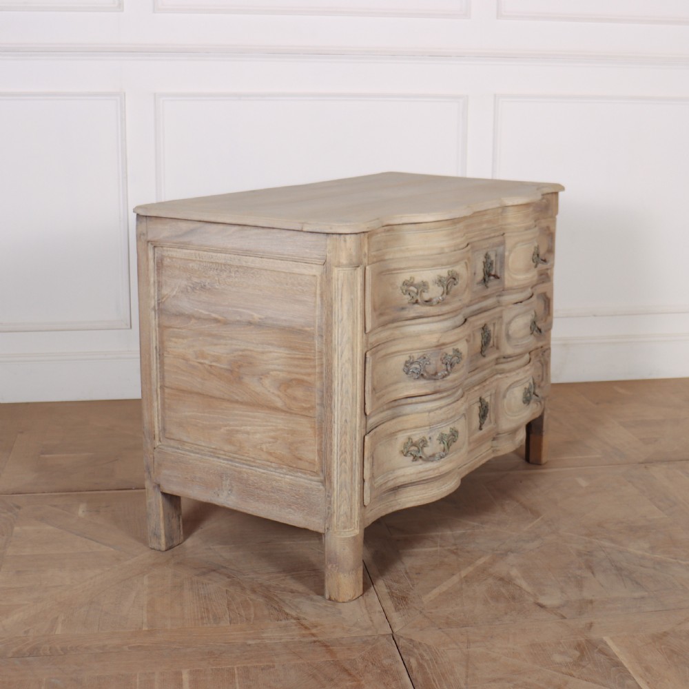 An 18th-century bleached oak French commode with three moulded serpentine drawers featuring brass handles and key escutcheons. View V
