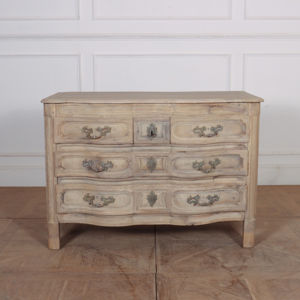 An 18th-century bleached oak French commode with three moulded serpentine drawers featuring brass handles and key escutcheons. View VI