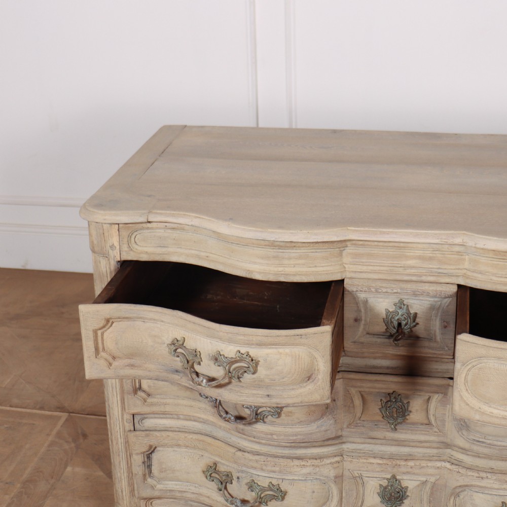 An 18th-century bleached oak French commode with three moulded serpentine drawers featuring brass handles and key escutcheons. View VIII