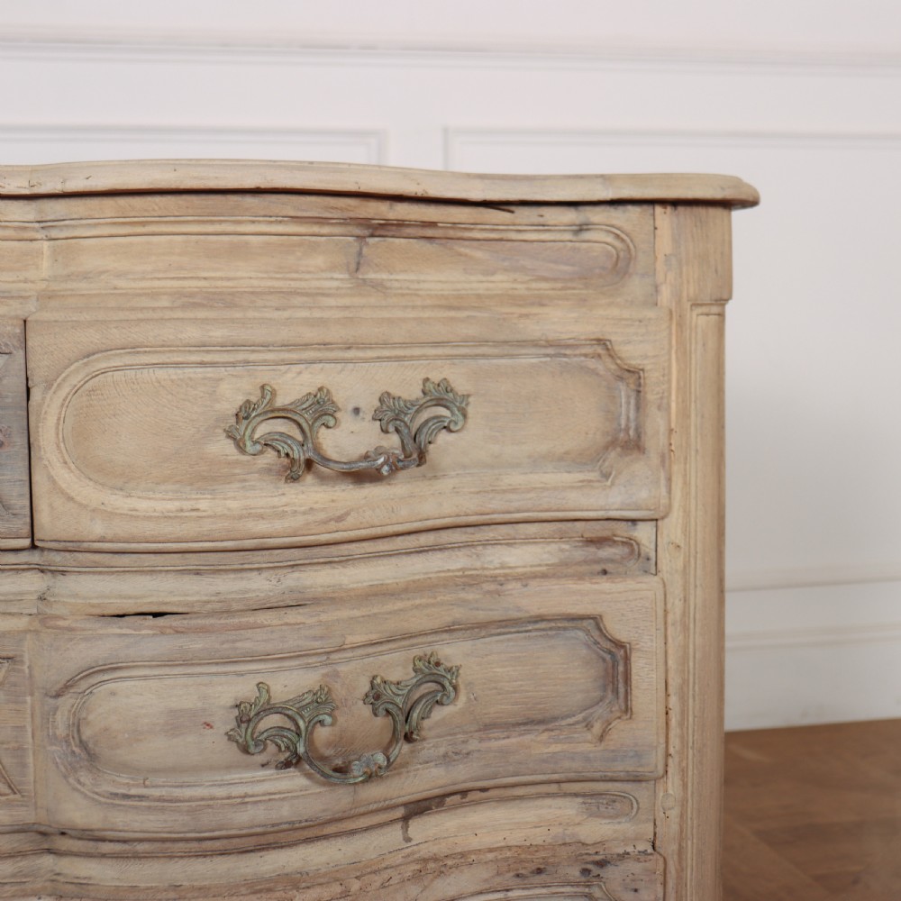 An 18th-century bleached oak French commode with three moulded serpentine drawers featuring brass handles and key escutcheons. View IX