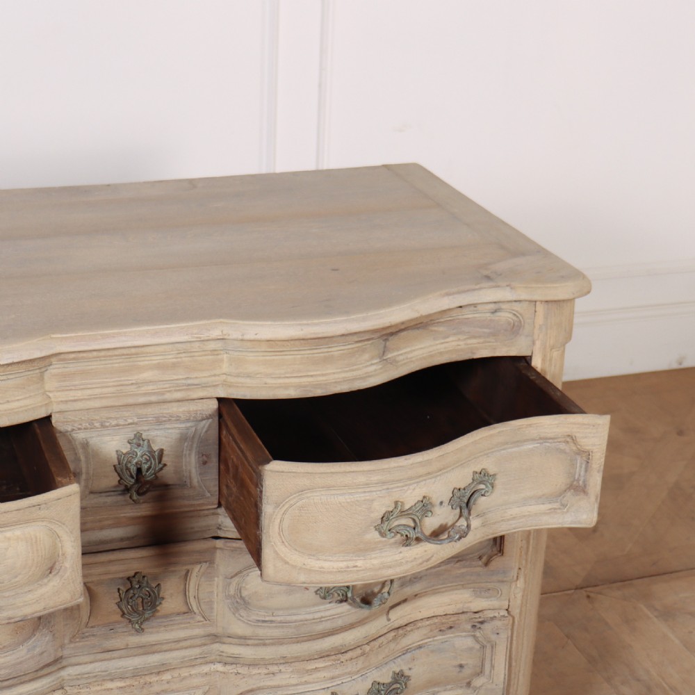 An 18th-century bleached oak French commode with three moulded serpentine drawers featuring brass handles and key escutcheons. View X