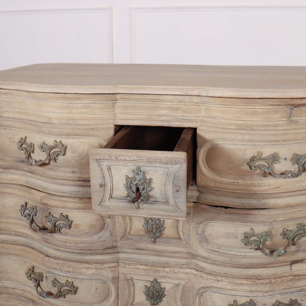 An 18th-century bleached oak French commode with three moulded serpentine drawers featuring brass handles and key escutcheons. View XI
