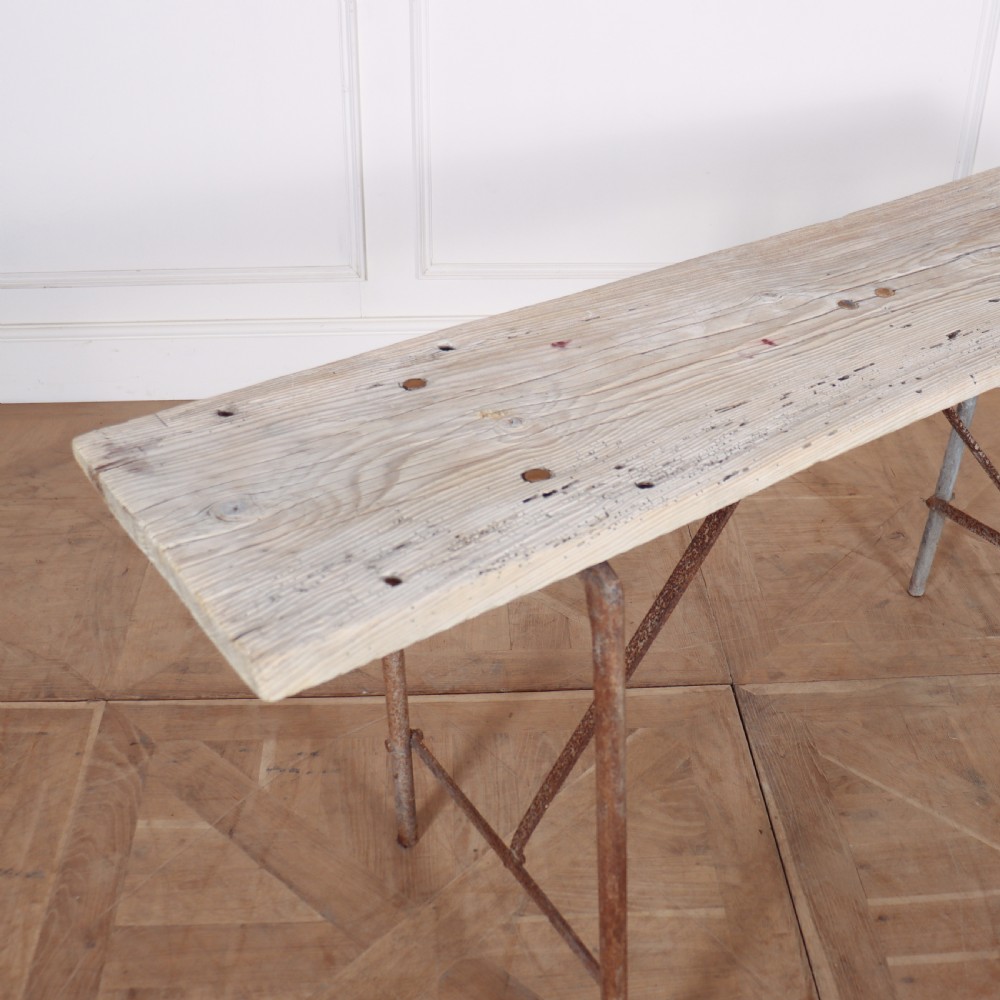 A long, narrow bleached timber top resting on a slender, oxidised metal trestle frame. View II