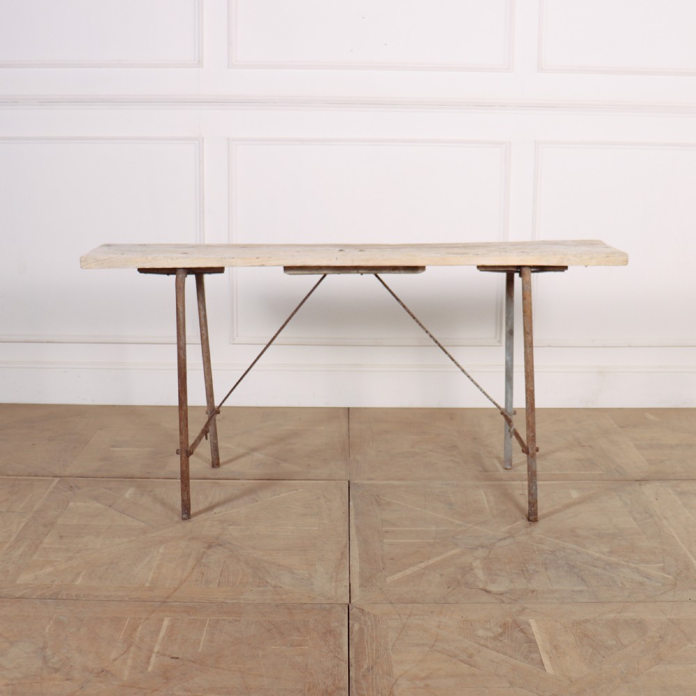 A long, narrow bleached timber top resting on a slender, oxidised metal trestle frame. View III