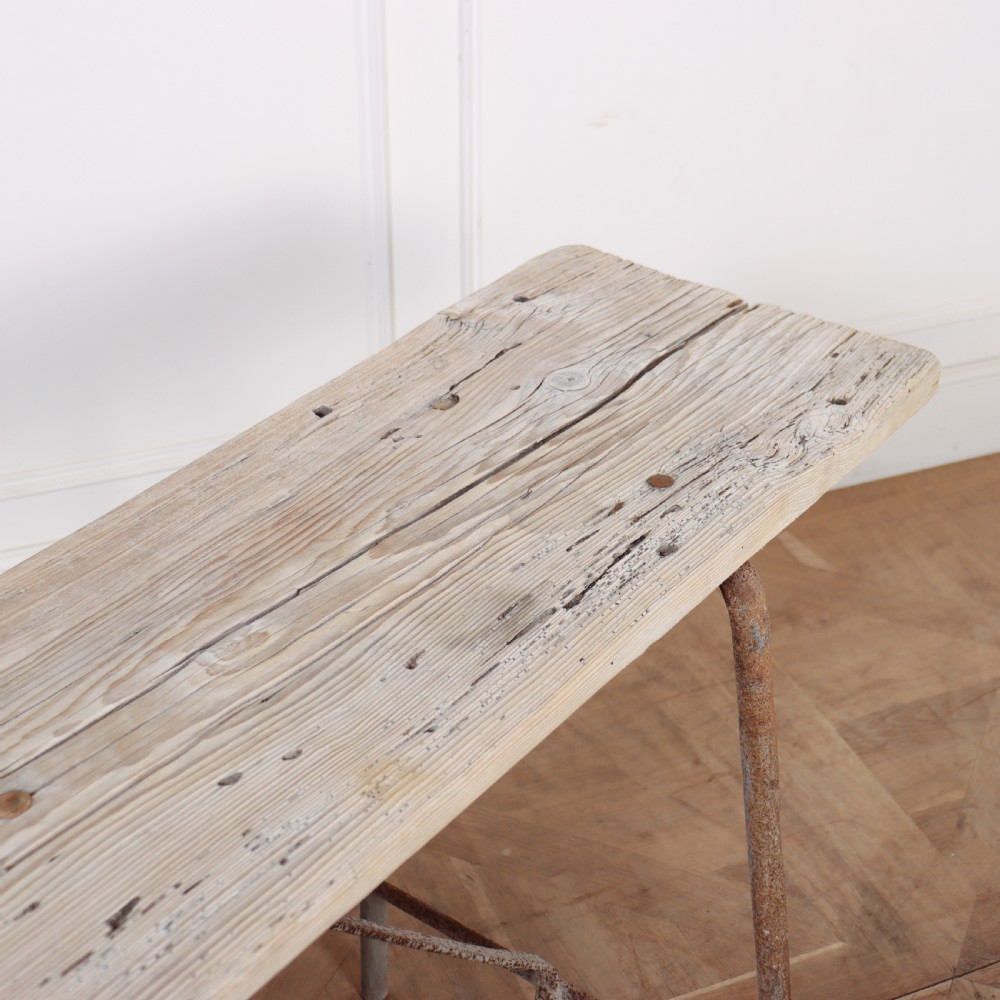 A long, narrow bleached timber top resting on a slender, oxidised metal trestle frame. View IV