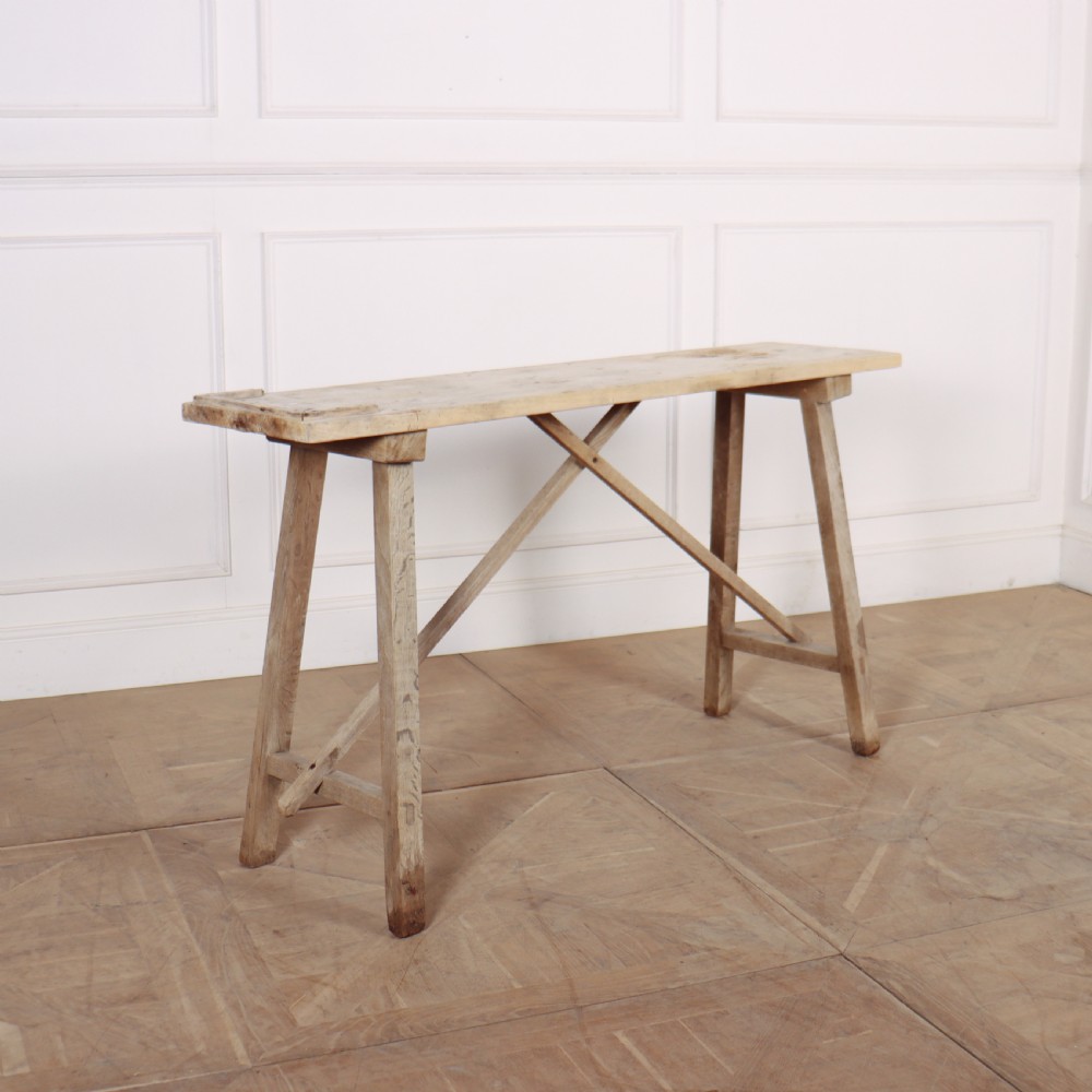 A narrow French bleached oak trestle table featuring a slim rectangular timber top supported by angled trestle legs with diagonal cross bracing.