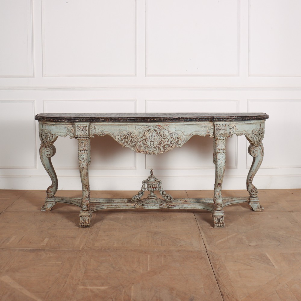A carved Spanish console table featuring distressed pale blue paintwork, a dark rectangular top, an intricate carved apron, and a central urn finial stretcher.