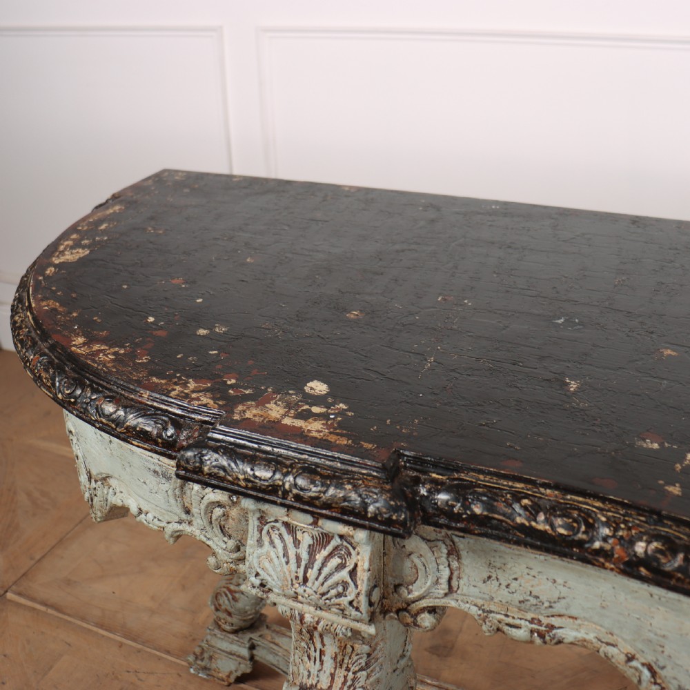 A carved Spanish console table featuring distressed pale blue paintwork, a dark rectangular top, an intricate carved apron, and a central urn finial stretcher. View IX