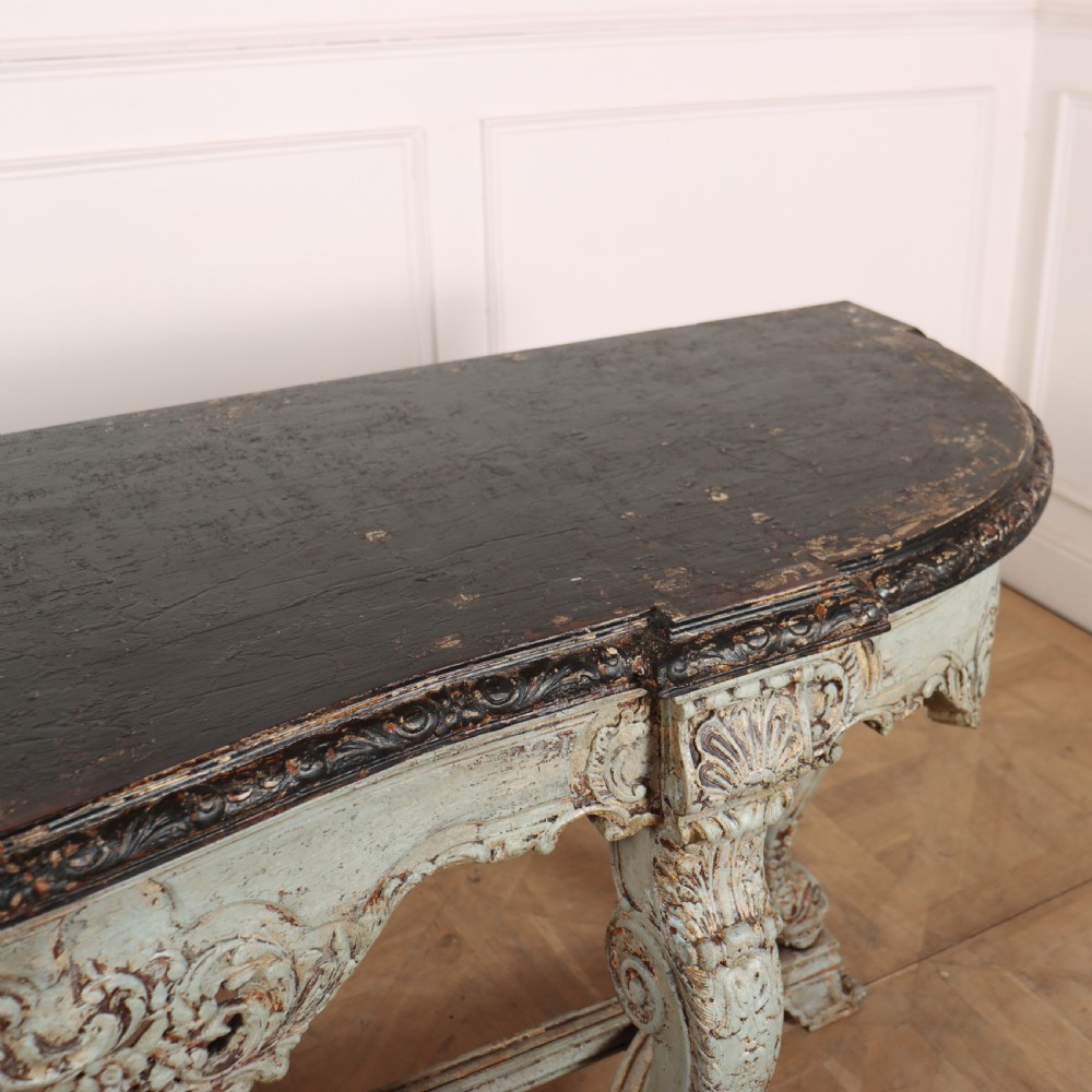 A carved Spanish console table featuring distressed pale blue paintwork, a dark rectangular top, an intricate carved apron, and a central urn finial stretcher. View X