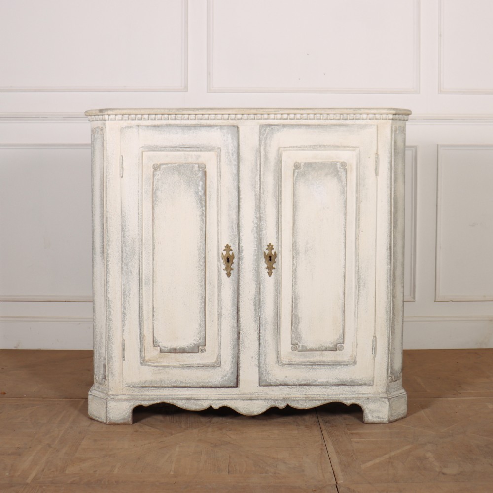 An 18th-century Swedish painted wooden linen cupboard featuring panelled double doors, brass keyhole escutcheons, and a distressed off-white painted finish.