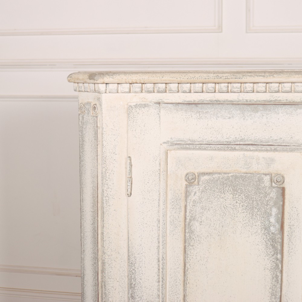 An 18th-century Swedish painted wooden linen cupboard featuring panelled double doors, brass keyhole escutcheons, and a distressed off-white painted finish. View II