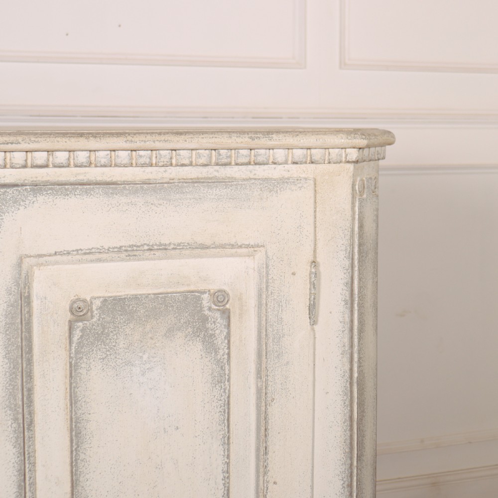 An 18th-century Swedish painted wooden linen cupboard featuring panelled double doors, brass keyhole escutcheons, and a distressed off-white painted finish. View III