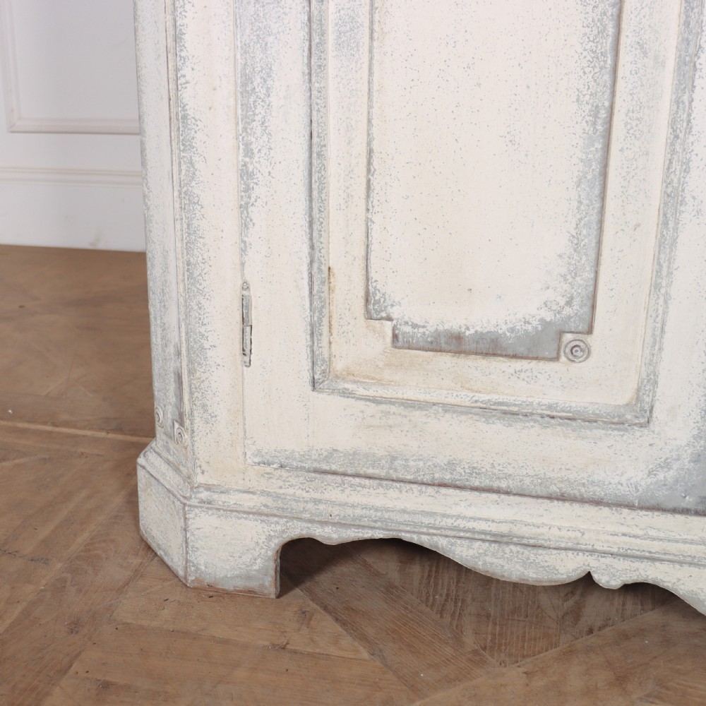 An 18th-century Swedish painted wooden linen cupboard featuring panelled double doors, brass keyhole escutcheons, and a distressed off-white painted finish. View V