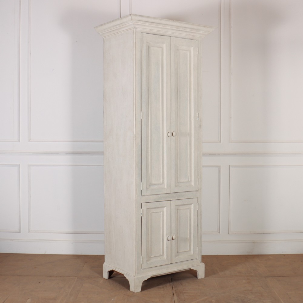A tall, narrow off-white painted pine linen cupboard featuring two upper panelled doors and two lower panelled doors with turned wooden knobs.