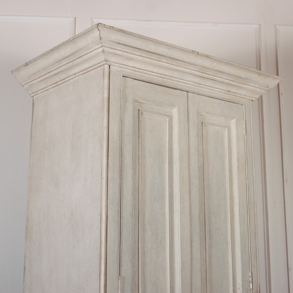 A tall, narrow off-white painted pine linen cupboard featuring two upper panelled doors and two lower panelled doors with turned wooden knobs. View II