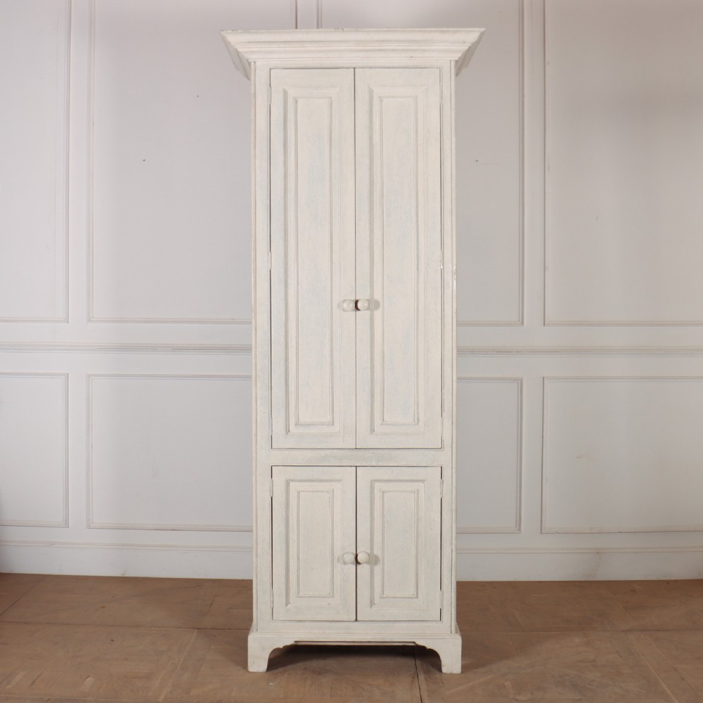 A tall, narrow off-white painted pine linen cupboard featuring two upper panelled doors and two lower panelled doors with turned wooden knobs. View III