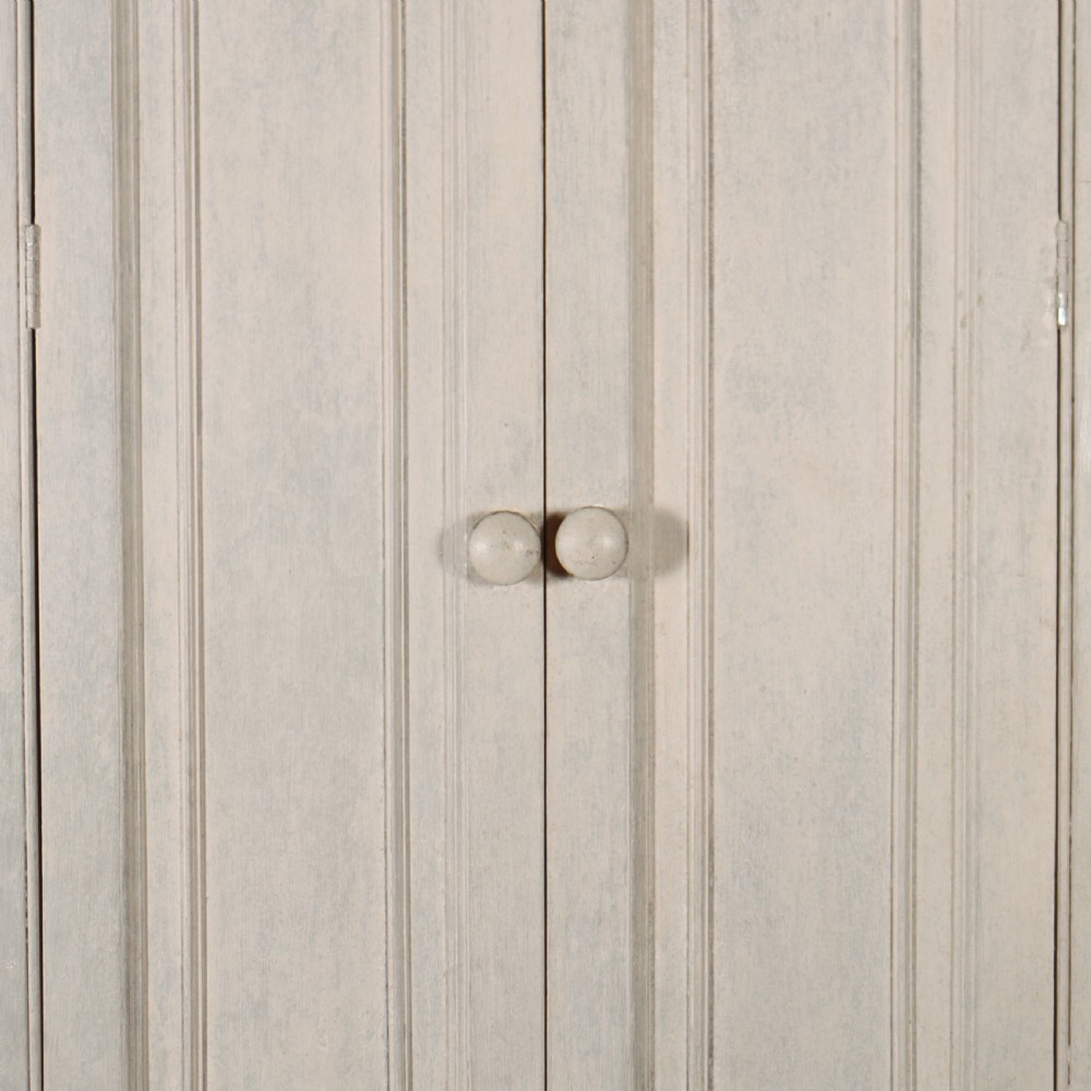A tall, narrow off-white painted pine linen cupboard featuring two upper panelled doors and two lower panelled doors with turned wooden knobs. View IV
