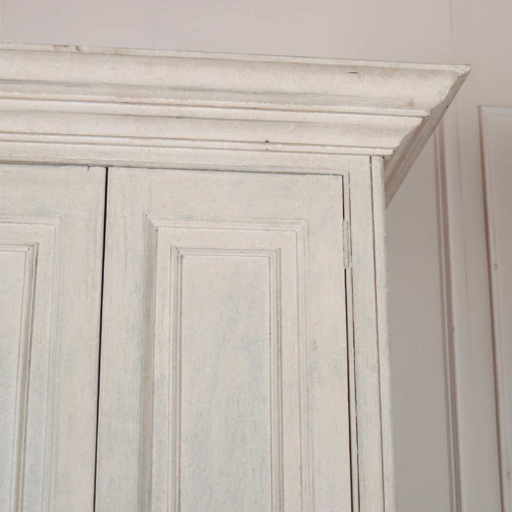 A tall, narrow off-white painted pine linen cupboard featuring two upper panelled doors and two lower panelled doors with turned wooden knobs. View VII