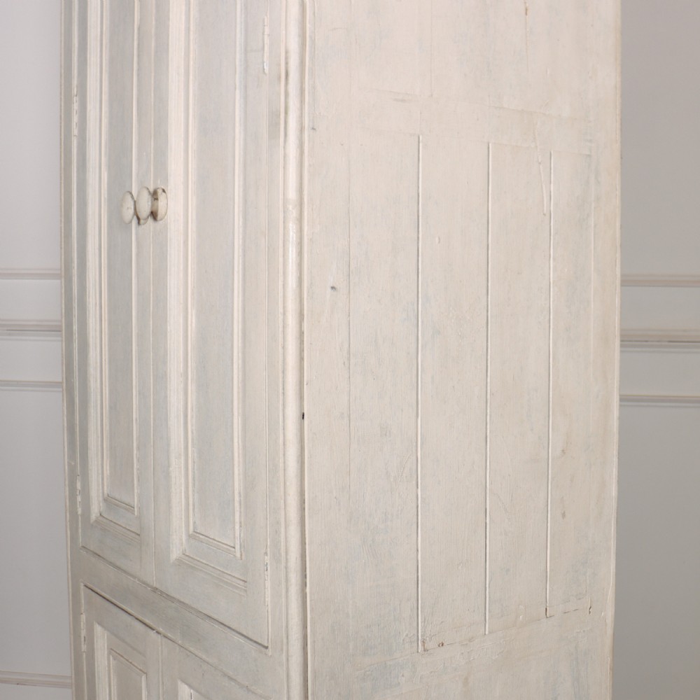 A tall, narrow off-white painted pine linen cupboard featuring two upper panelled doors and two lower panelled doors with turned wooden knobs. View VIII
