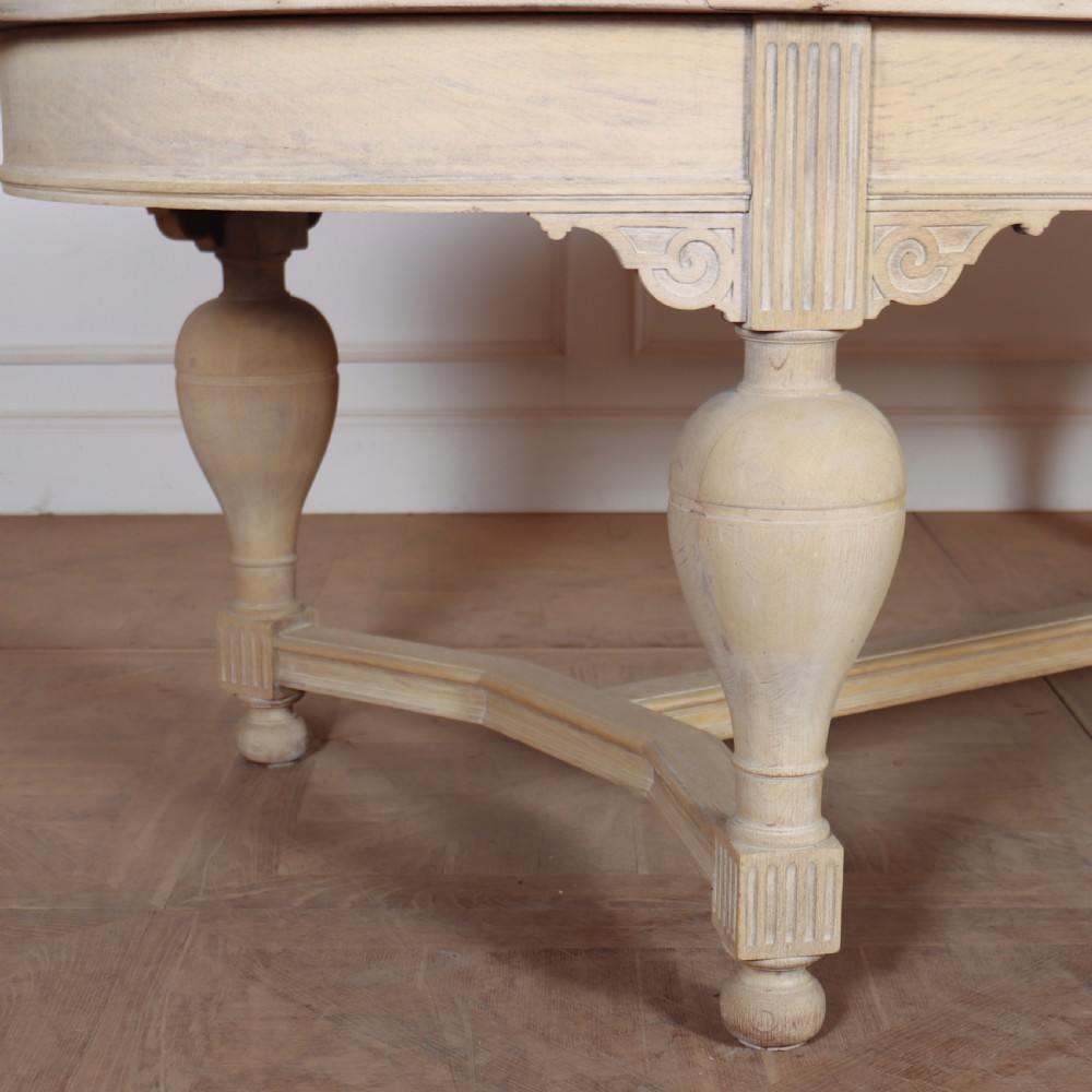 An oval bleached oak dining table featuring carved corner brackets, turned baluster legs, and a low H-stretcher base. View II