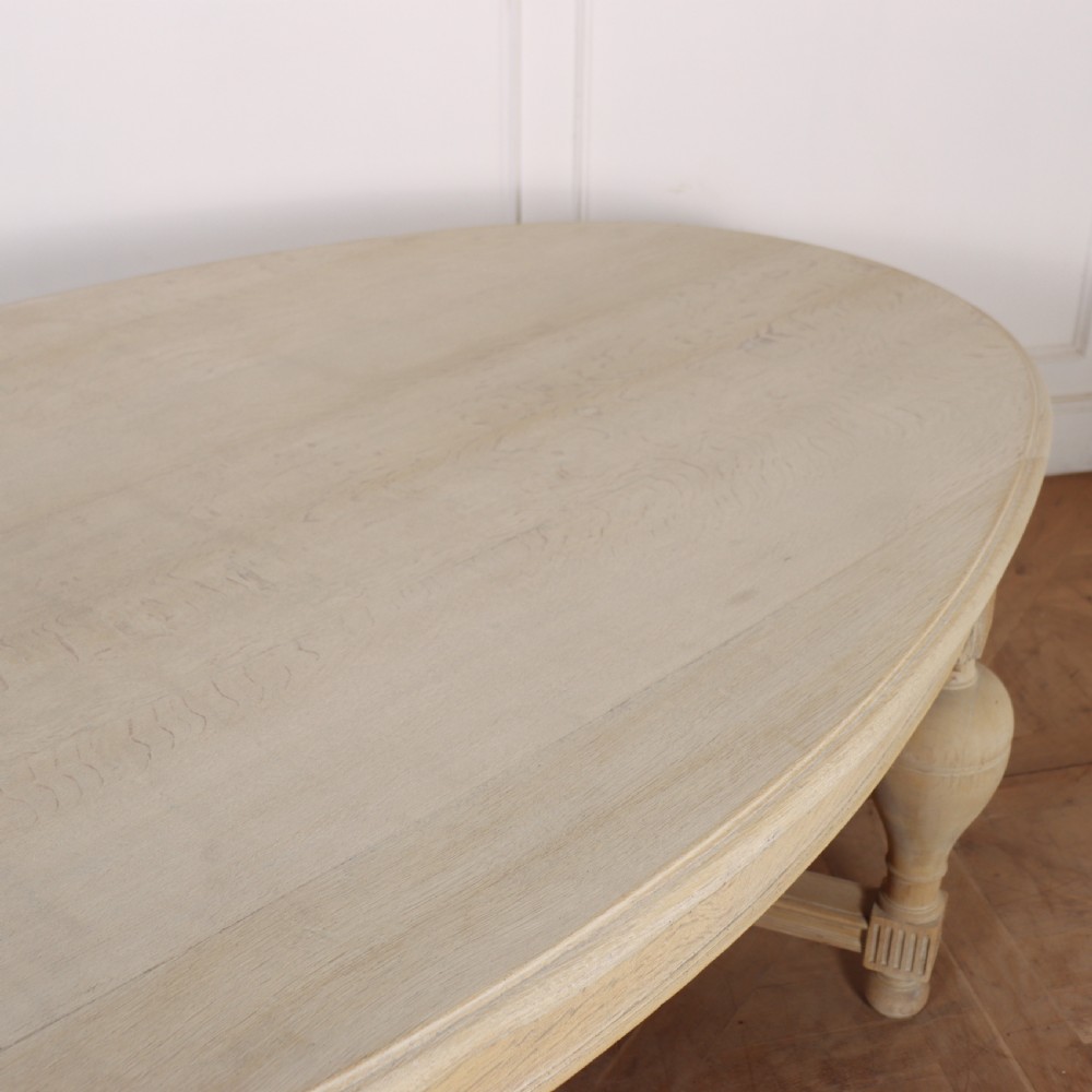 An oval bleached oak dining table featuring carved corner brackets, turned baluster legs, and a low H-stretcher base. View III