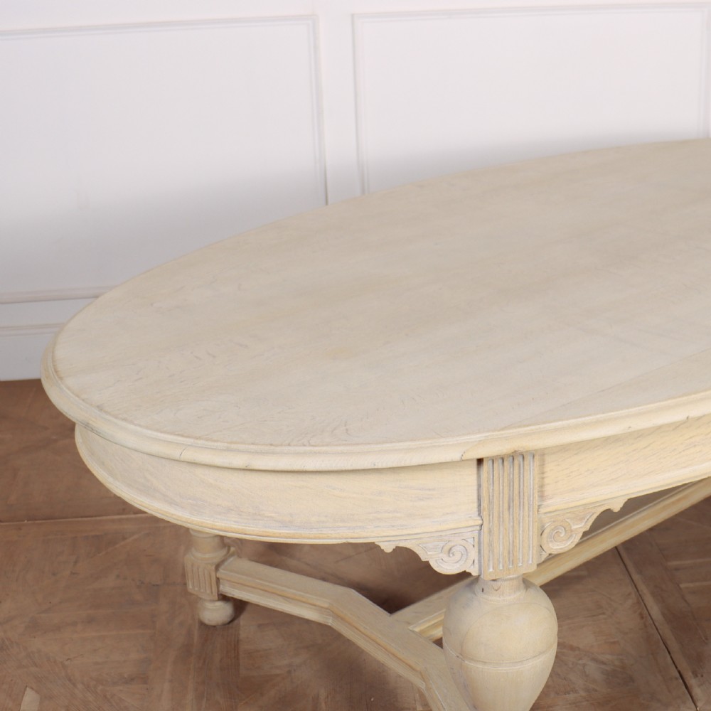 An oval bleached oak dining table featuring carved corner brackets, turned baluster legs, and a low H-stretcher base. View IV
