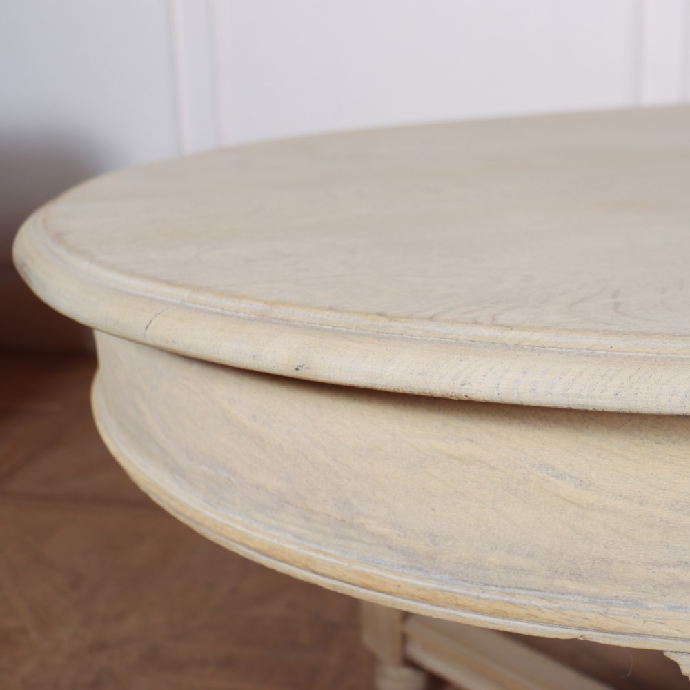 An oval bleached oak dining table featuring carved corner brackets, turned baluster legs, and a low H-stretcher base. View V