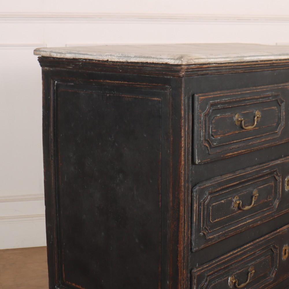 An 18th-century French painted black commode featuring three long drawers with moulded panels, brass drop handles, and a grey marble top. View III