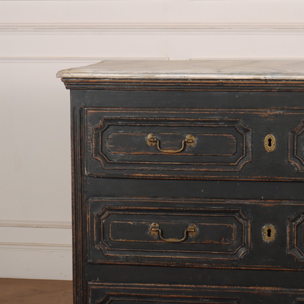 An 18th-century French painted black commode featuring three long drawers with moulded panels, brass drop handles, and a grey marble top. View V