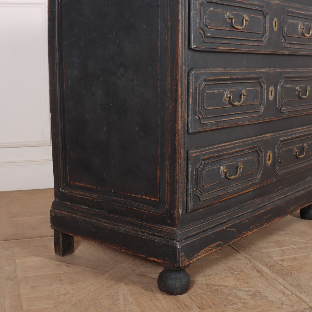 An 18th-century French painted black commode featuring three long drawers with moulded panels, brass drop handles, and a grey marble top. View VI