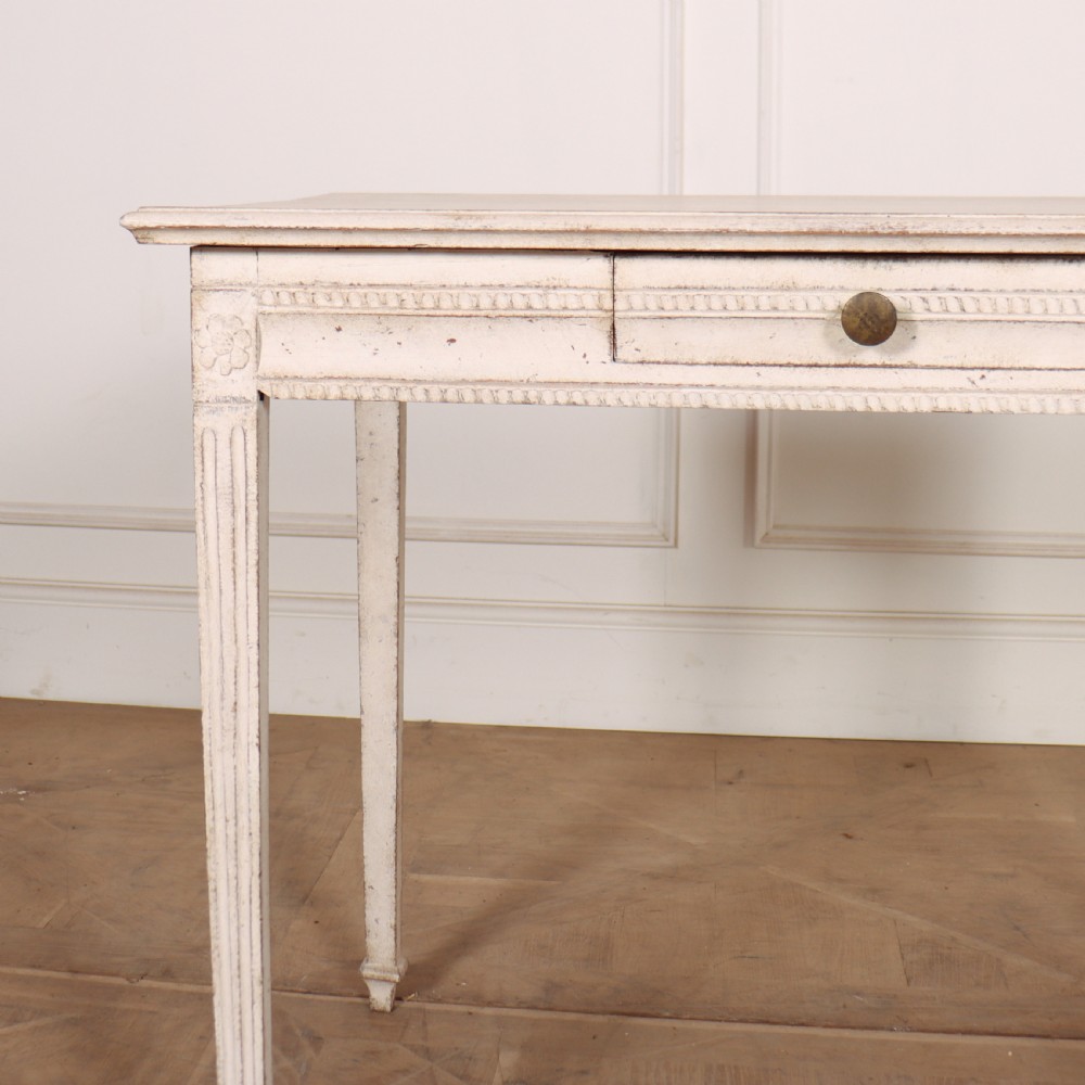 An off-white painted Swedish Gustavian side table featuring slim fluted legs, carved corner rosettes, and a single frieze drawer with a brass pull knob. View II