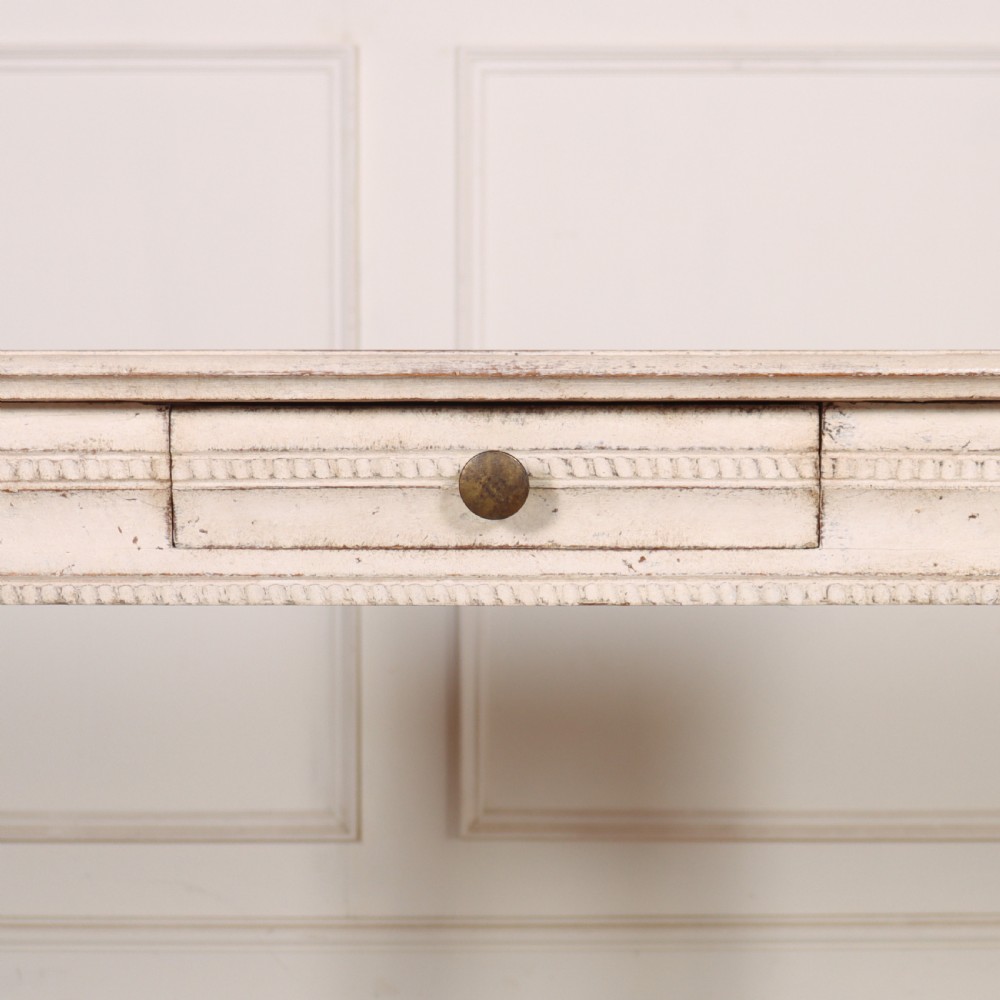 An off-white painted Swedish Gustavian side table featuring slim fluted legs, carved corner rosettes, and a single frieze drawer with a brass pull knob. View IV