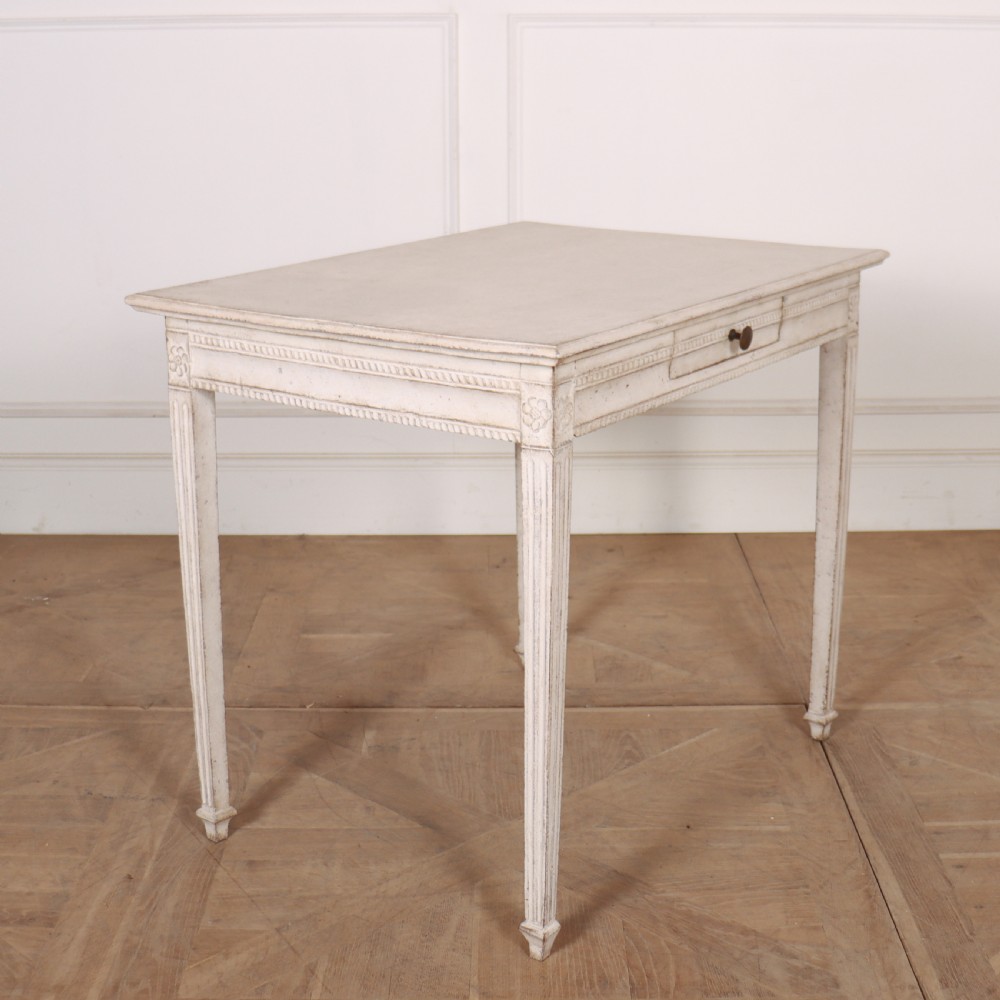 An off-white painted Swedish Gustavian side table featuring slim fluted legs, carved corner rosettes, and a single frieze drawer with a brass pull knob. View V