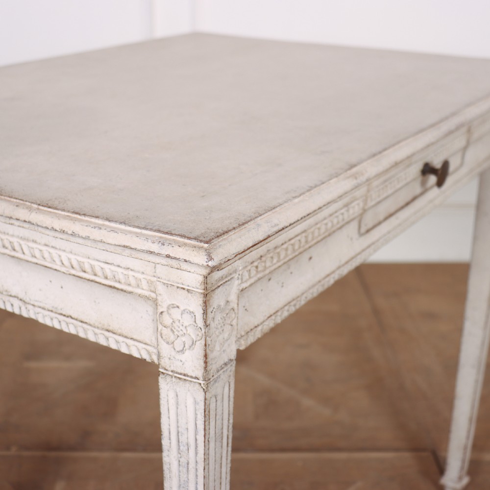 An off-white painted Swedish Gustavian side table featuring slim fluted legs, carved corner rosettes, and a single frieze drawer with a brass pull knob. View VI