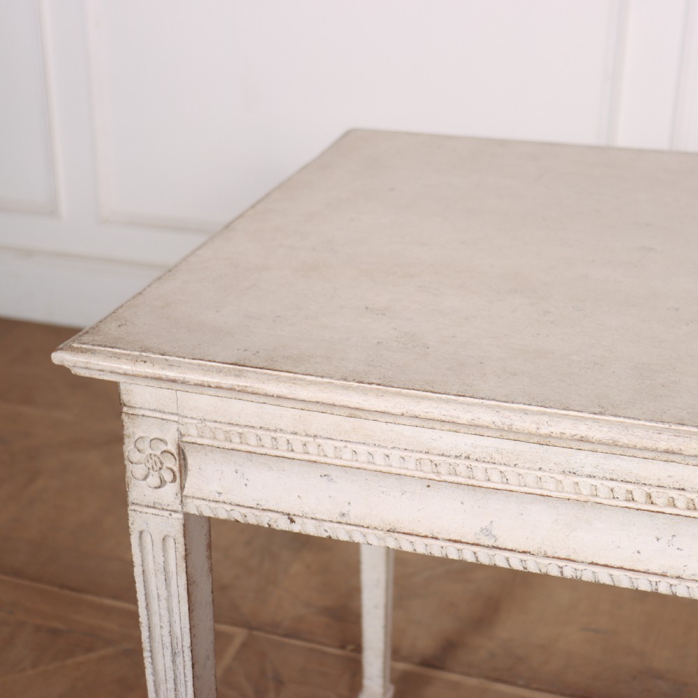 An off-white painted Swedish Gustavian side table featuring slim fluted legs, carved corner rosettes, and a single frieze drawer with a brass pull knob. View VII