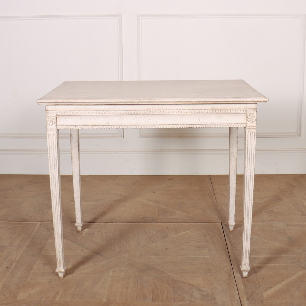 An off-white painted Swedish Gustavian side table featuring slim fluted legs, carved corner rosettes, and a single frieze drawer with a brass pull knob. View VIII