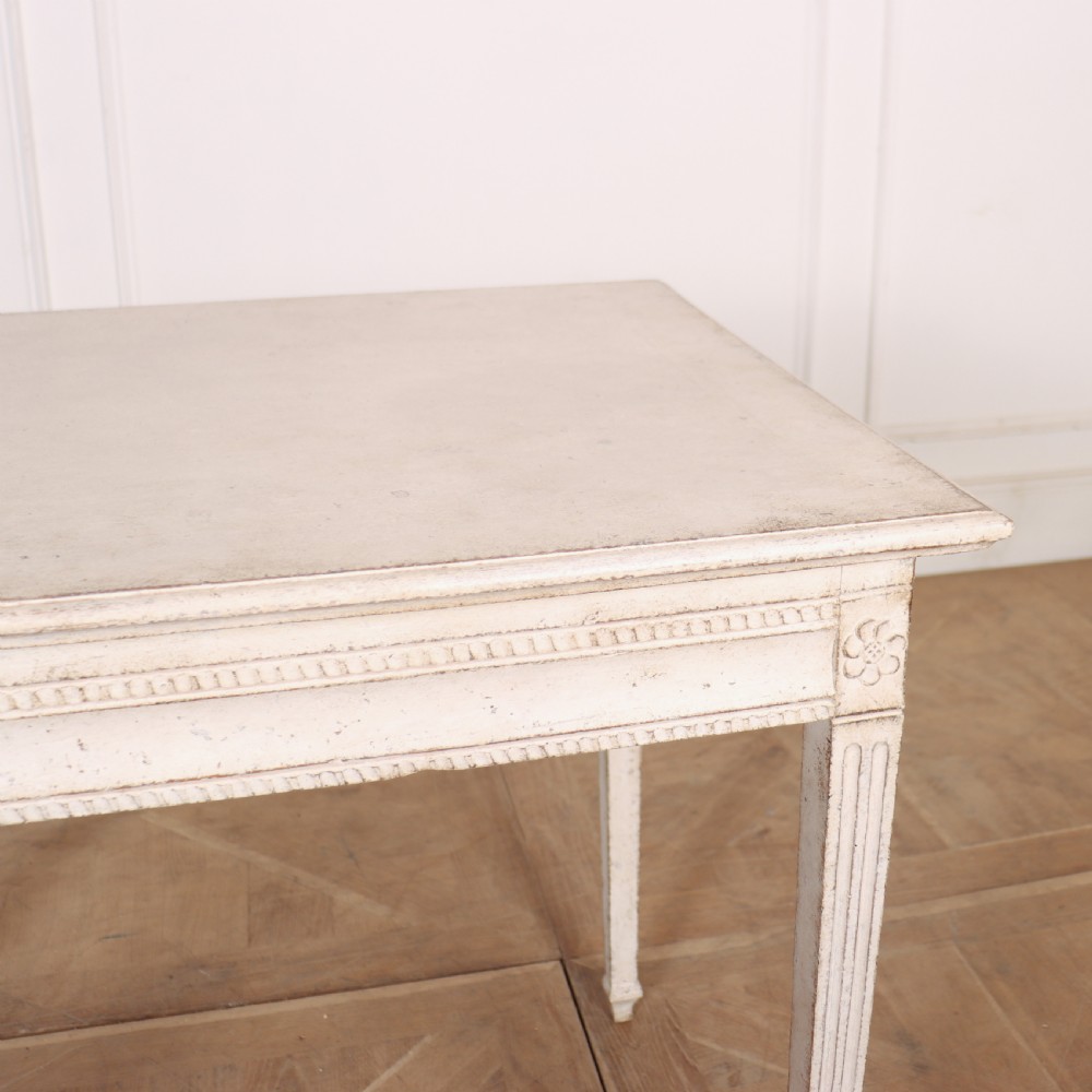An off-white painted Swedish Gustavian side table featuring slim fluted legs, carved corner rosettes, and a single frieze drawer with a brass pull knob. View IX