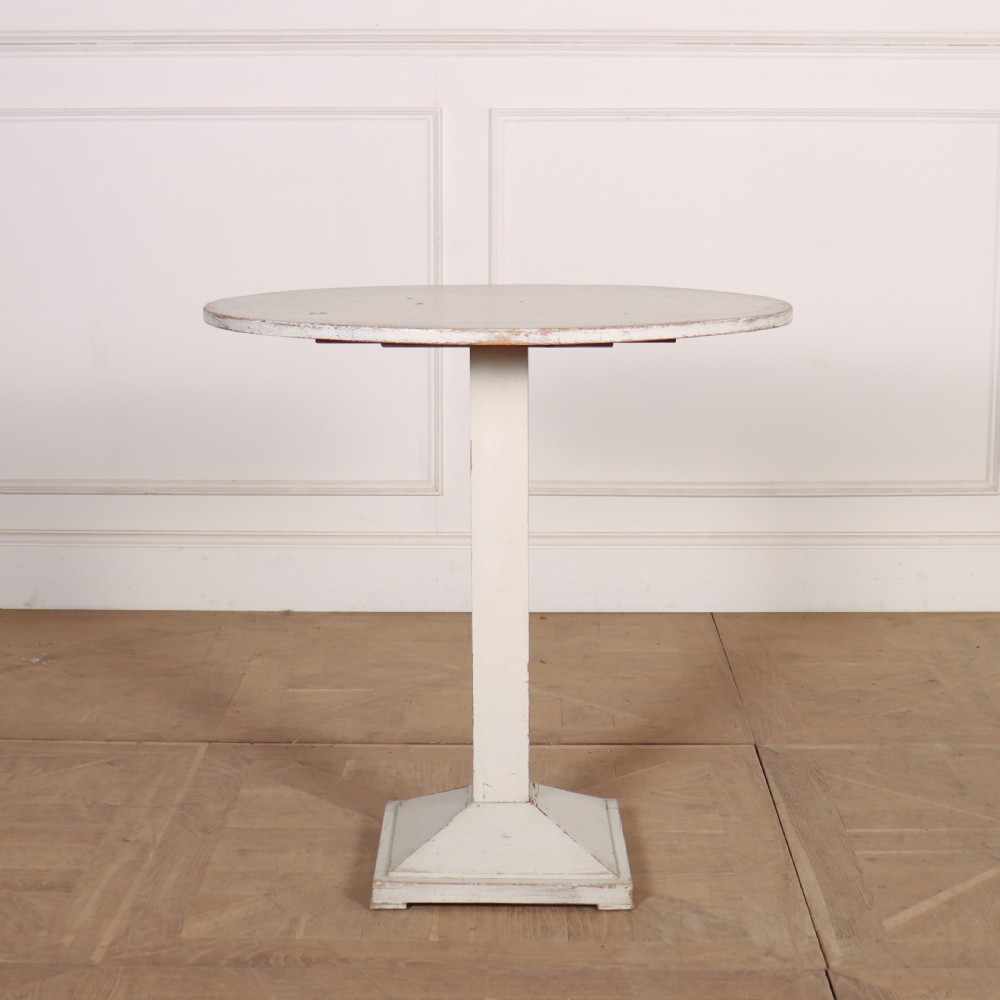 An off-white painted Swedish pedestal table featuring a circular top, a square central column, and a stepped plinth base with visible paint wear along the edges.