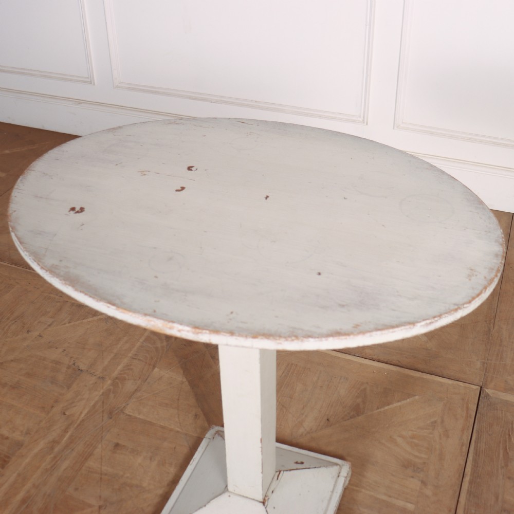 An off-white painted Swedish pedestal table featuring a circular top, a square central column, and a stepped plinth base with visible paint wear along the edges. View III