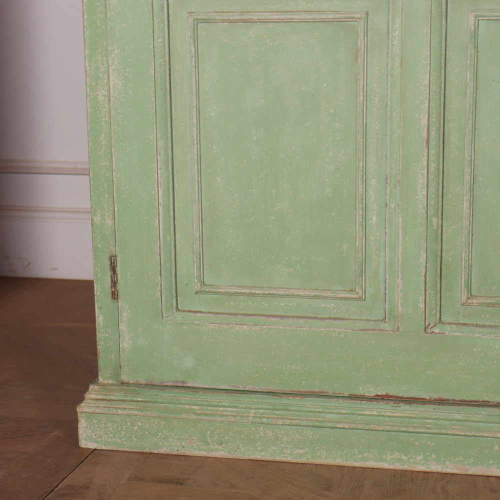 A low sage green painted wooden linen cupboard with three panelled doors and a dark wood top. View III
