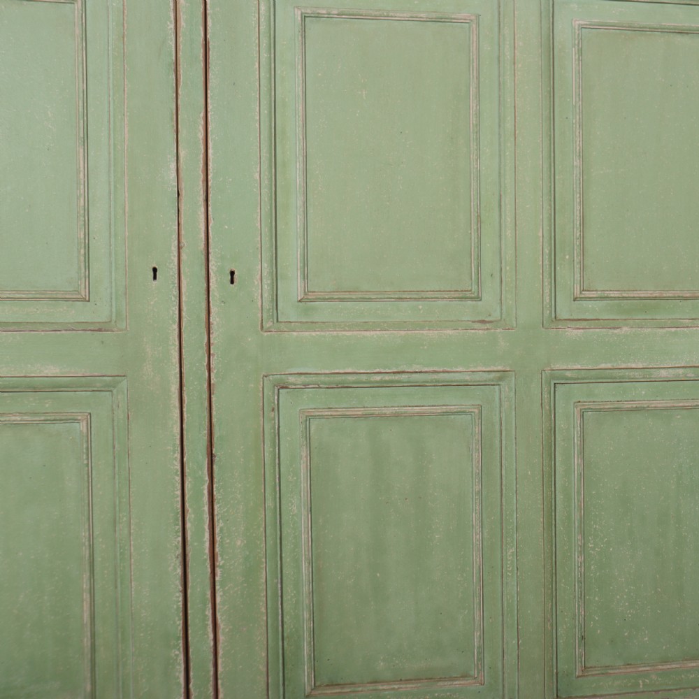 A low sage green painted wooden linen cupboard with three panelled doors and a dark wood top. View IV