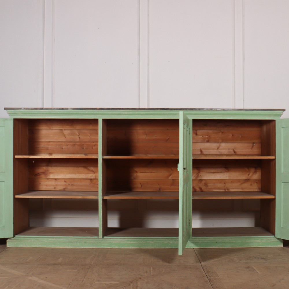 A low sage green painted wooden linen cupboard with three panelled doors and a dark wood top. View V