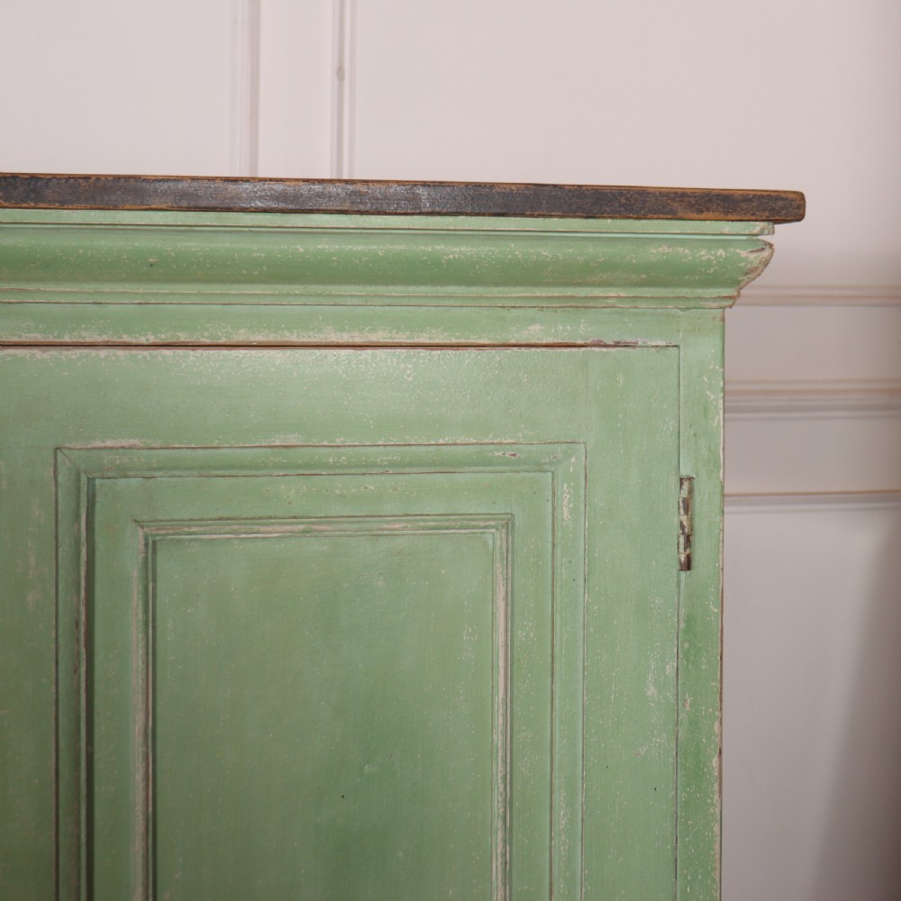 A low sage green painted wooden linen cupboard with three panelled doors and a dark wood top. View VI