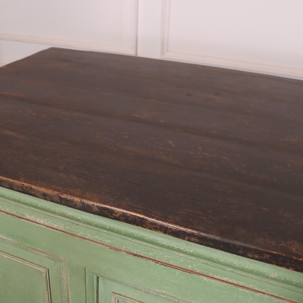 A low sage green painted wooden linen cupboard with three panelled doors and a dark wood top. View VII