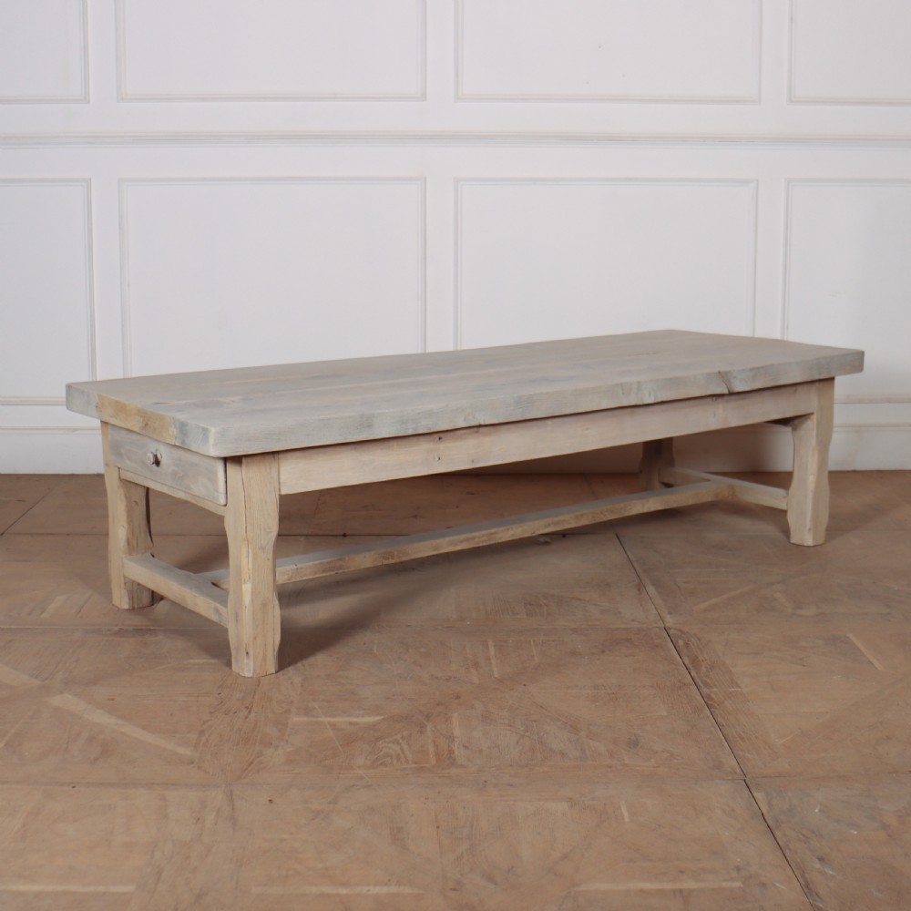 A low rectangular French coffee table constructed from bleached oak, featuring a thick plank top, square legs, a low stretcher, and a small end drawer.