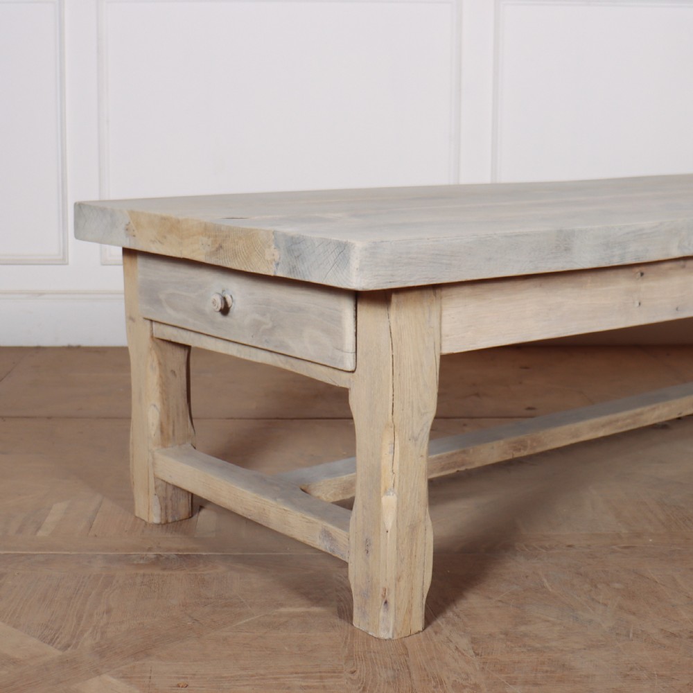 A low rectangular French coffee table constructed from bleached oak, featuring a thick plank top, square legs, a low stretcher, and a small end drawer. View II
